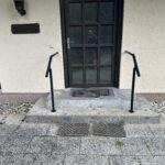 Schwarz geölter Handlauf aus Stahl an einer Außentreppe mit Natursteinstufen vor einem Hauseingang