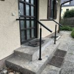 Schwarz geölter Handlauf aus Stahl an einer Außentreppe mit Natursteinstufen vor einem Hauseingang